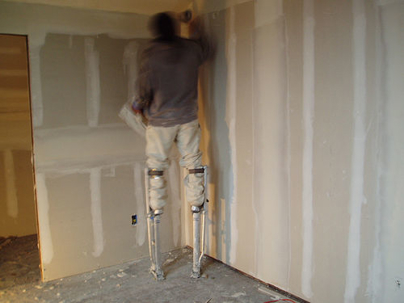 a man on stilts working on drywall