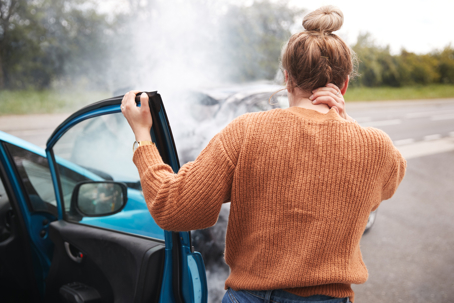 A woman stands by her car after a wreck, holding her neck