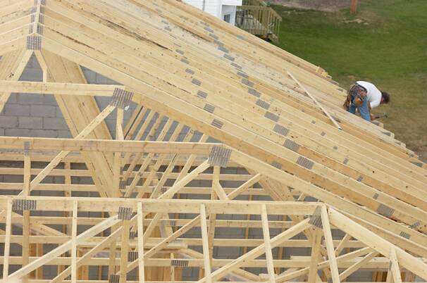 A construction worker installs the roof framing on a house.