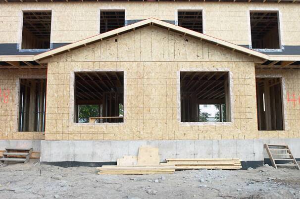 A building under construction features a foundation, wood framing, and a window opening.