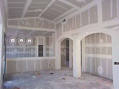 An interior view of an unfinished room shows walls covered in drywall with an arched doorway.